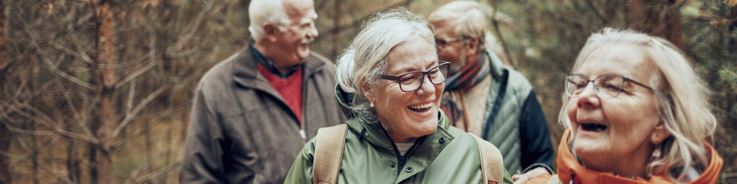 Neljä ikääntyvää, hymyilevää ihmistä kävelee metsässä.