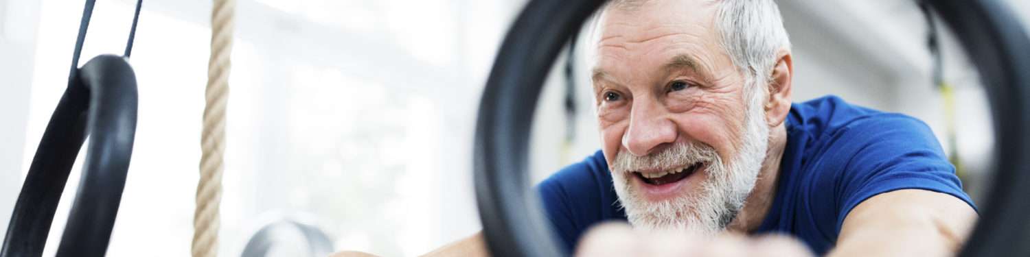 Iäkäs, hymyilevä, harmaahiuksinen parrakas mies pitää kiinni voimistelurenkaista.