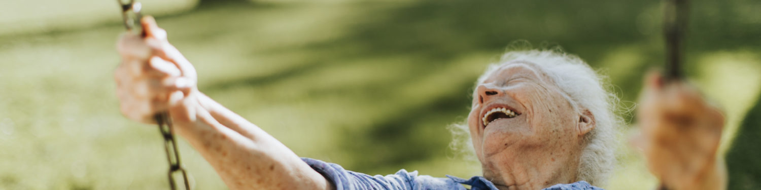 Iäkäs, harmaahiuksinen nainen keinuu silmät kiinni hymyillen.